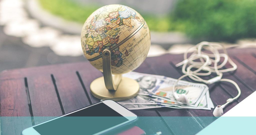 Foto eines Globus auf dem Schreibtisch mit Smartphone, Stift, Geld und Kopfhörern in der Nähe