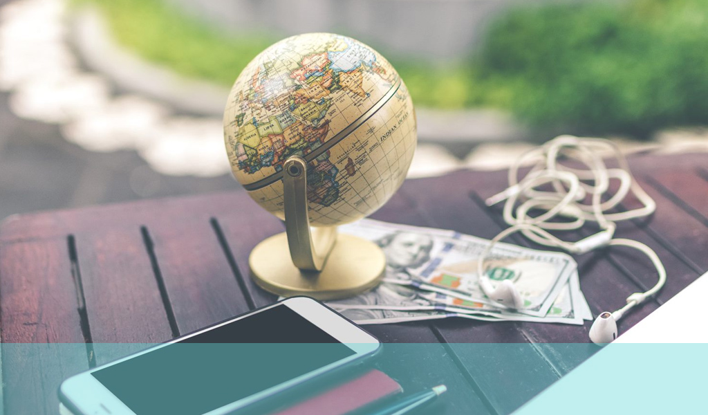 Foto eines Globus auf dem Schreibtisch mit Smartphone, Stift, Geld und Kopfhörern in der Nähe